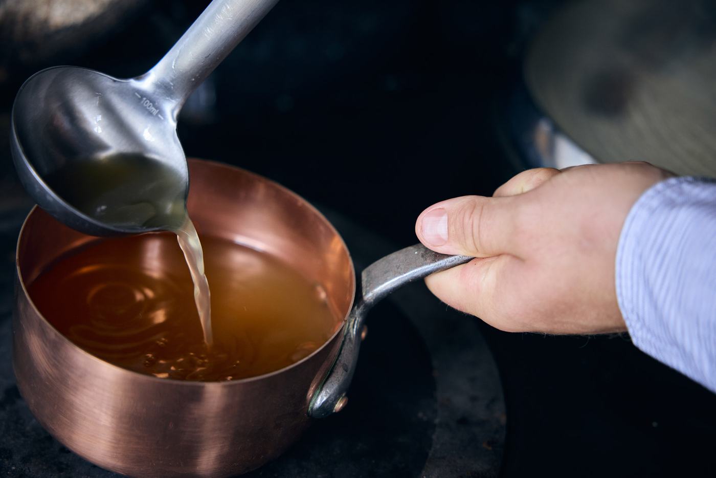 Golden chicken bone broth being ladled into a copper pan