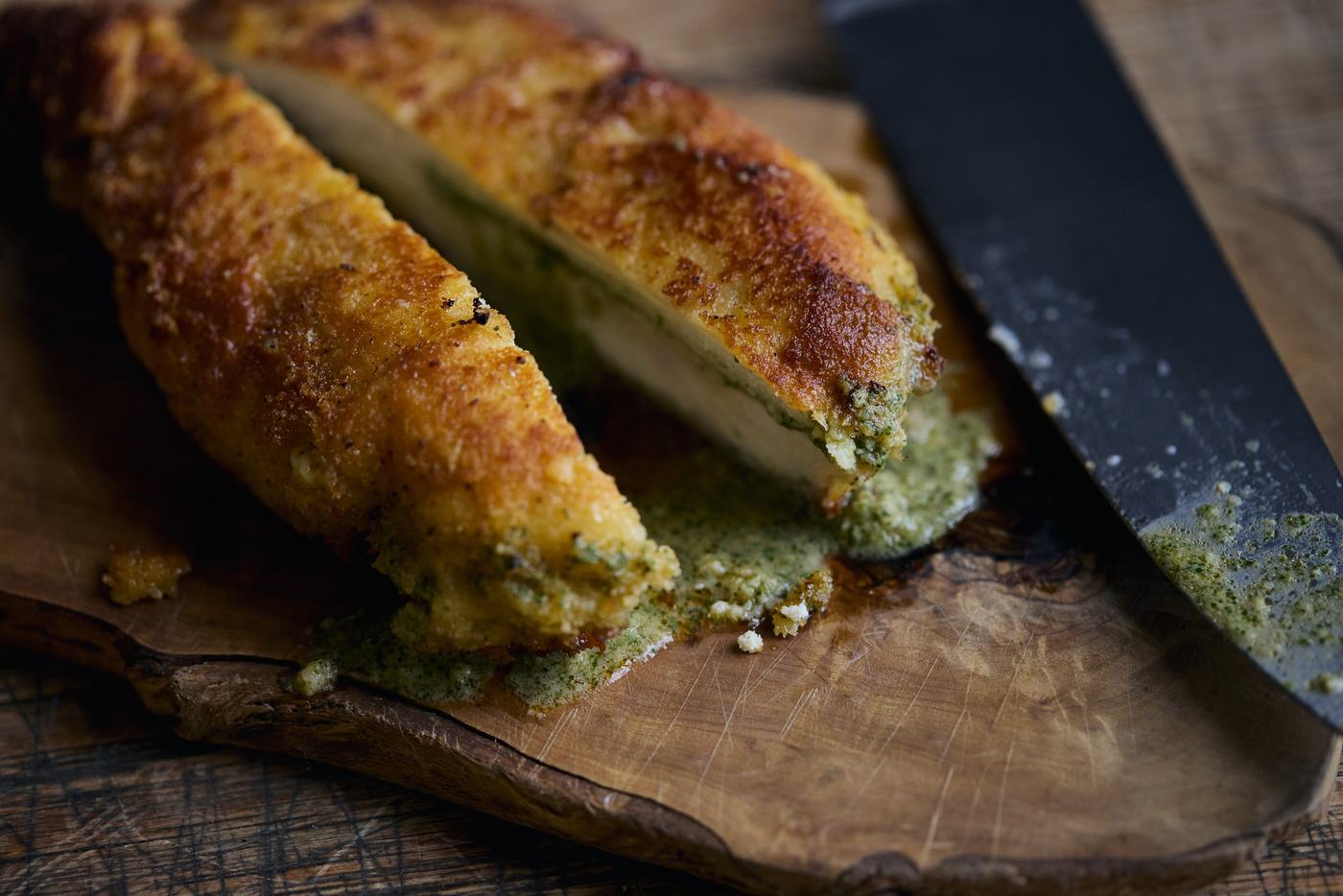 Sliced golden chicken kiev with garlic-herb butter on a wooden board