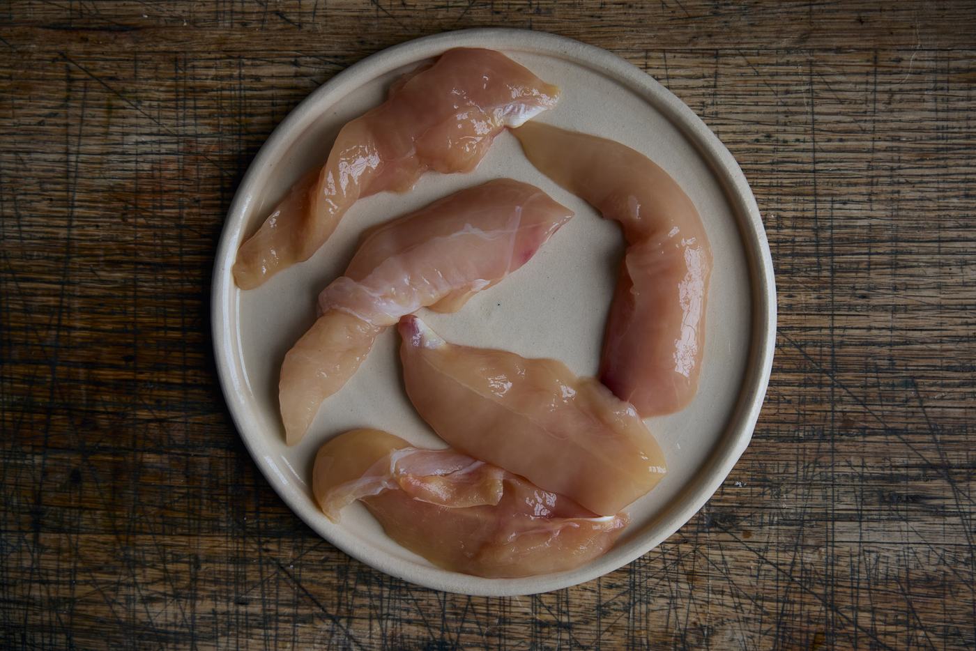 Raw chicken mini fillets on a ceramic plate