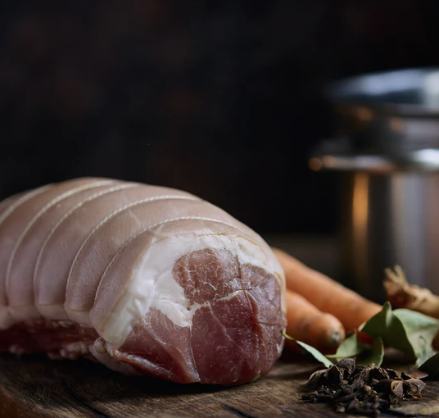 Dry cured rolled gammon joint on a wooden board with carrots and bay