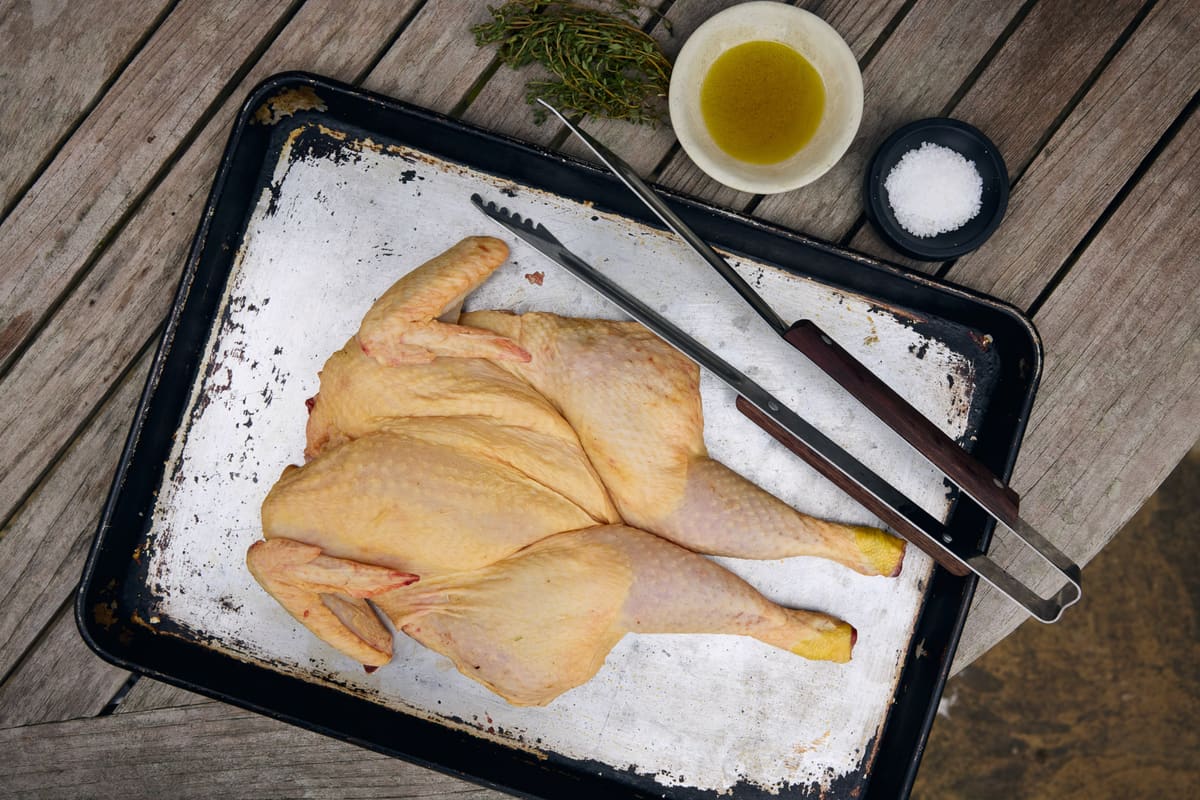 Spatchcocked chicken on an enamel tray with thyme, oil and sea salt