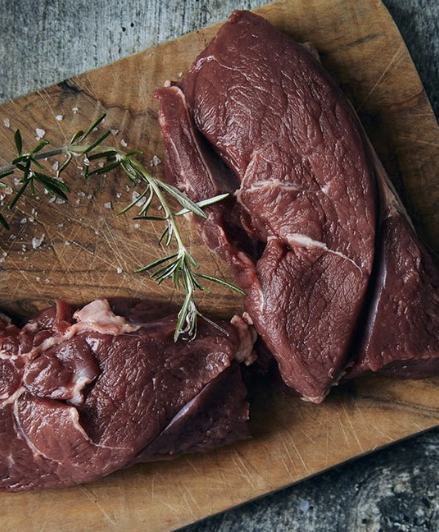 Wild venison haunch steaks with rosemary on a wooden board