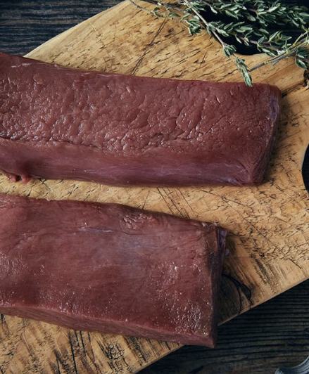 Wild venison loin steaks on a wooden board with thyme